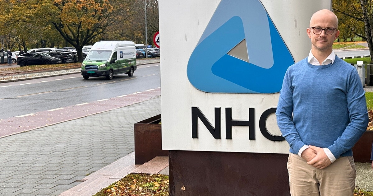 To personer foran NHOs logo ved Næringslivets Hus