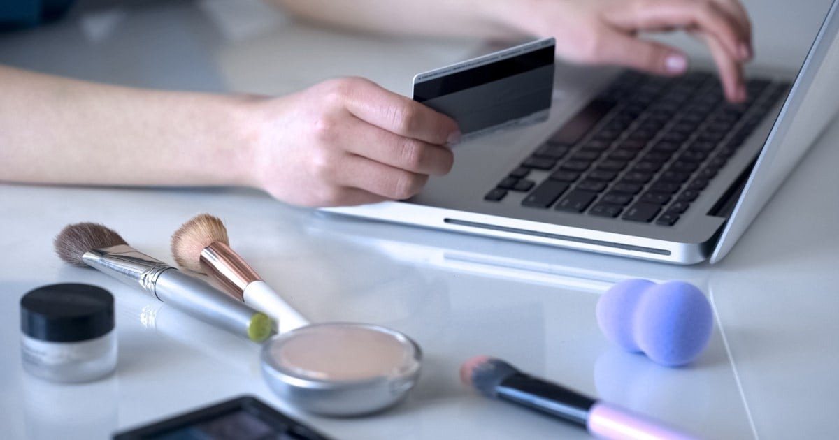 kosmetikkprodukter ved siden av laptop og hender som holder et kredittkort.